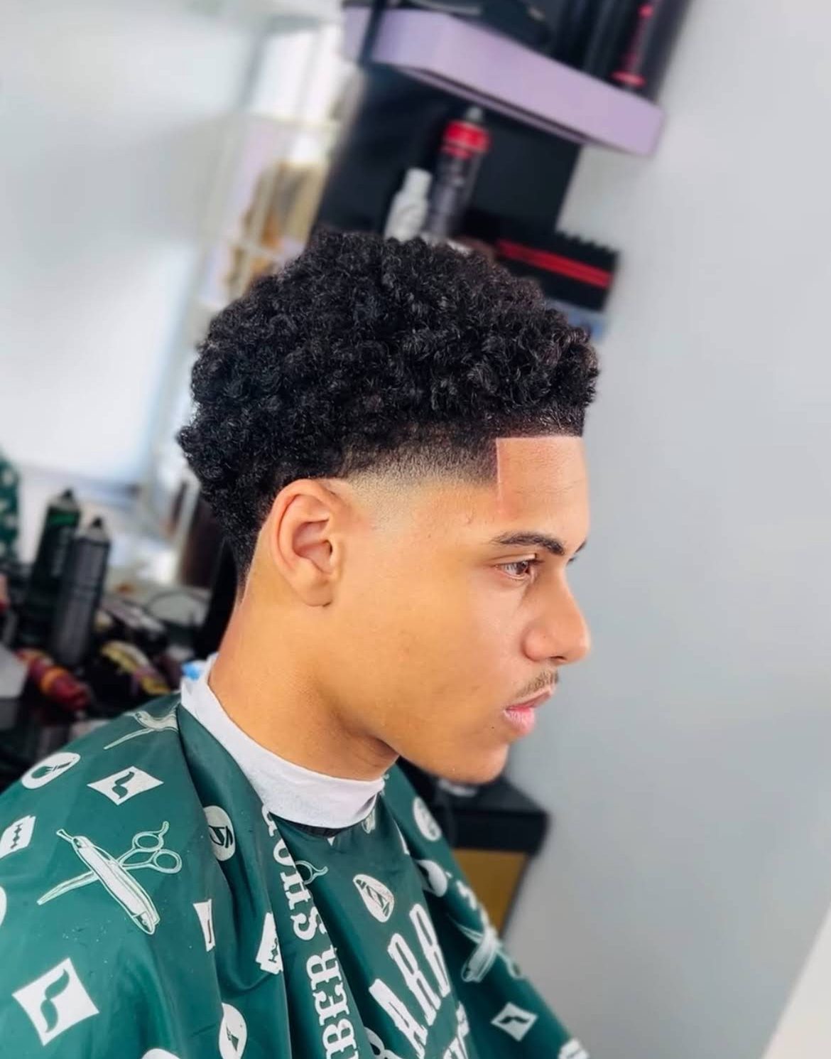 Taper fade with defined curls on top, side profile